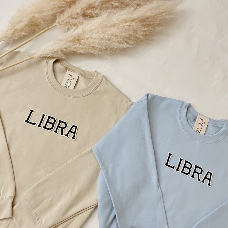 May include: Two sweatshirts with the word "LIBRA" embroidered on the front. One sweatshirt is beige and the other is light blue.