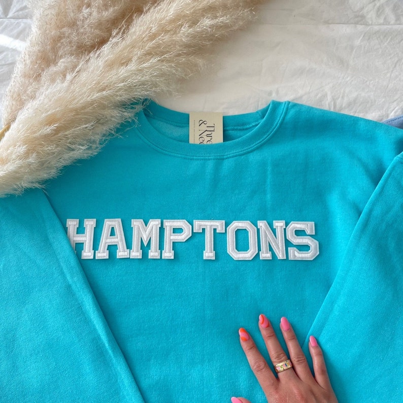 May include: A turquoise blue sweatshirt with white embroidered lettering that reads "HAMPTONS".