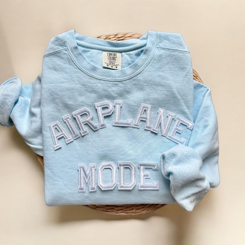K&ouml;nnte beinhalten: Ein hellblauer Pullover mit den Worten "AIRPLANE MODE" in wei&szlig;en umrandeten Buchstaben.