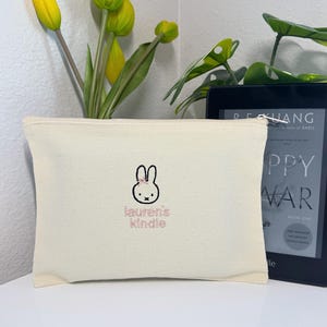 May include: A white canvas pouch with a pink embroidered bunny and the text "lauren's kindle".
