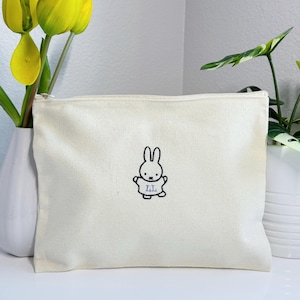 May include: A white canvas zippered pouch with a black embroidered image of a bunny wearing a shirt with the letters "LL" on it.