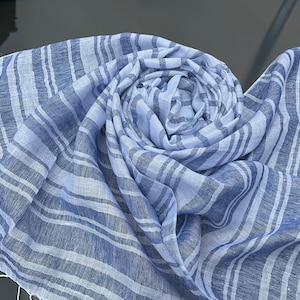 Könnte beinhalten: Gerollter Schal mit blau-weißen Streifen und Fransen. Der Schal besteht aus einem leichten Stoff mit abwechselnden hellblauen und weißen Streifen. Der Schal ist ein vielseitiges Accessoire.