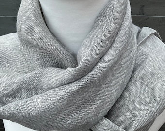 Puede incluir: Una bufanda de lino gris con tejido texturizado. La bufanda está doblada y drapeada sobre el cuello de un maniquí.
