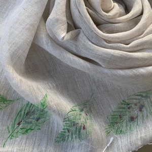 May include: A light beige linen scarf with a green fern pattern printed on the edge.