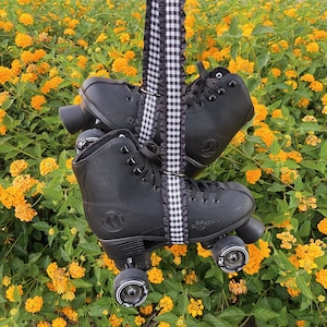 May include: Black roller skates with black and white checkered ribbon. The skates have black wheels and are set against a background of yellow flowers.