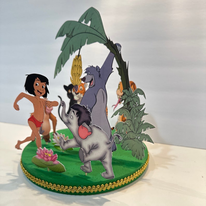 Peut inclure: Un topper de g&acirc;teau vert et or repr&eacute;sentant des personnages du Livre de la Jungle. Les personnages incluent Mowgli, Baloo, Shere Khan et Kaa. Le topper est en papier et est parfait pour une f&ecirc;te sur le th&egrave;me du Livre de la Jungle.