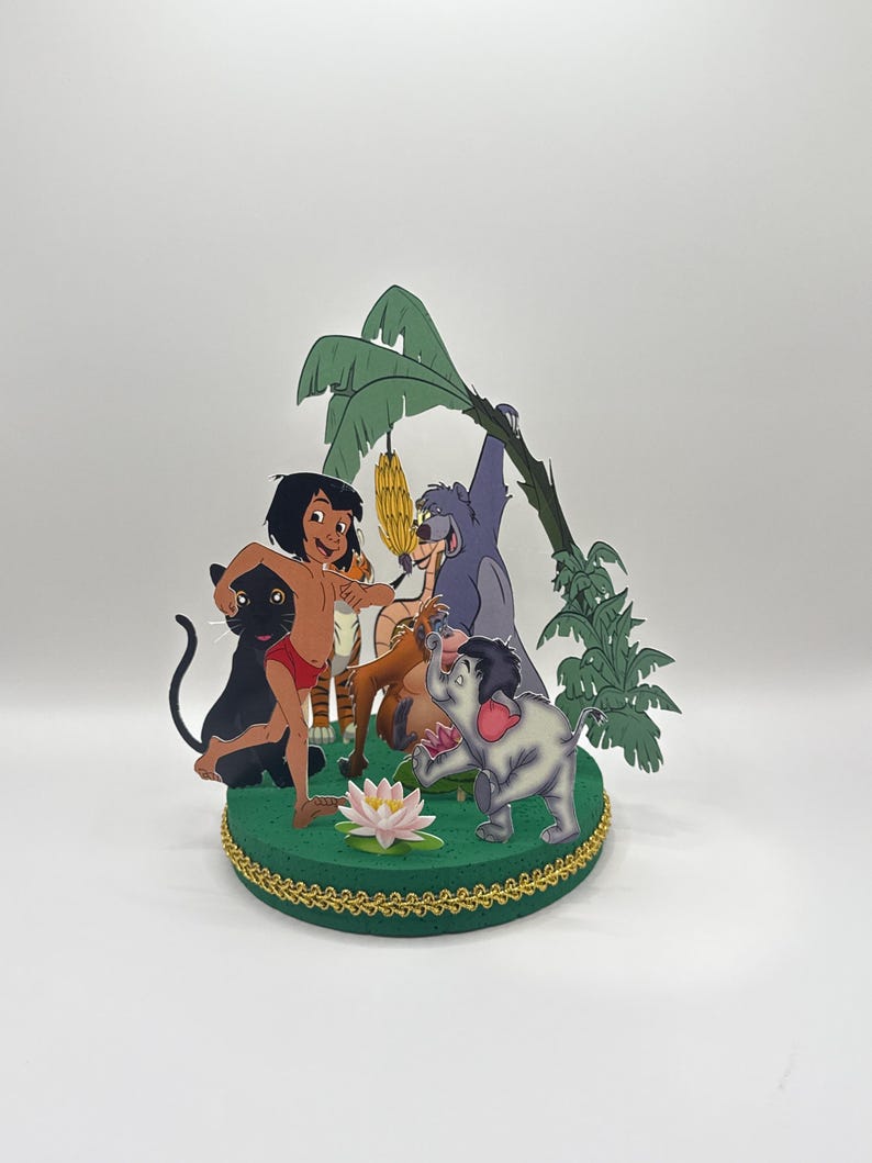 Peut inclure: Un topper de g&acirc;teau sur le th&egrave;me de la jungle vert et marron repr&eacute;sentant Mowgli du Livre de la Jungle de Disney. Le topper comprend Mowgli, Baloo l'ours, Bagheera la panth&egrave;re, Kaa le serpent et une fleur de lotus rose.