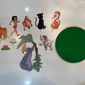 Peut inclure: Un ensemble de d&eacute;corations de g&acirc;teau sur le th&egrave;me du Livre de la Jungle avec des personnages comme Mowgli, Baloo, Shere Khan, King Louie, Kaa et Bagheera. Les d&eacute;corations sont imprim&eacute;es sur du papier cartonn&eacute; et ont un fond blanc.