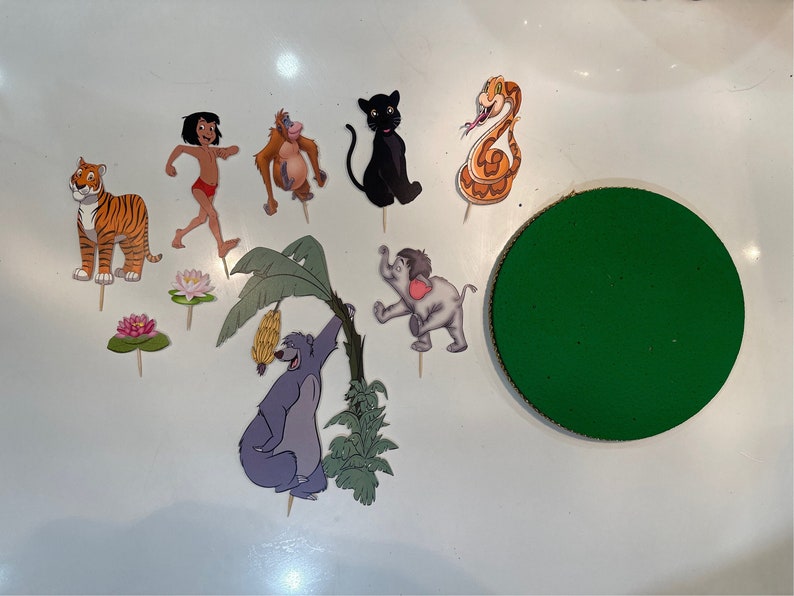 Peut inclure: Un ensemble de d&eacute;corations de g&acirc;teau sur le th&egrave;me du Livre de la Jungle avec des personnages comme Mowgli, Baloo, Shere Khan, King Louie, Kaa et Bagheera. Les d&eacute;corations sont imprim&eacute;es sur du papier cartonn&eacute; et ont un fond blanc.