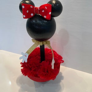 Pode incluir: Centro de mesa Minnie Mouse preto e vermelho com um la&ccedil;o vermelho, uma fita dourada e luvas brancas. A base &eacute; um c&iacute;rculo de espuma vermelha com cravos vermelhos.