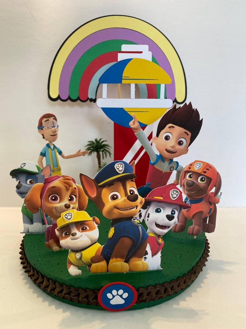 Puede incluir: Un adorno para pastel con tem&aacute;tica de la Patrulla Canina con los personajes Chase, Marshall, Skye, Rocky, Rubble y Ryder. El adorno incluye un arco&iacute;ris y un faro con una parte superior amarilla y azul.