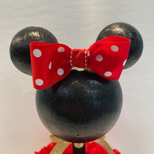 Pode incluir: Centro de mesa tem&aacute;tico do Mickey Mouse preto e vermelho com um la&ccedil;o vermelho com bolinhas brancas. O centro de mesa &eacute; feito de isopor e tem uma base vermelha e dourada.