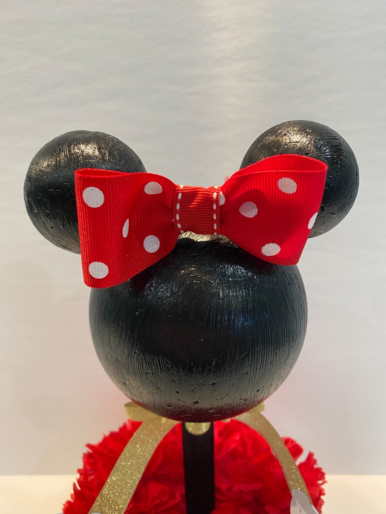 Pode incluir: Centro de mesa tem&aacute;tico do Mickey Mouse preto e vermelho com um la&ccedil;o vermelho com bolinhas brancas. O centro de mesa &eacute; feito de isopor e tem uma base vermelha e dourada.