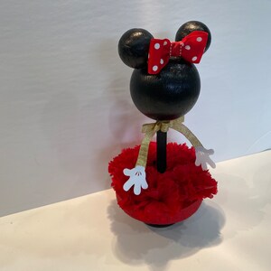 Pode incluir: Figura de Minnie Mouse preta e branca com um la&ccedil;o vermelho e uma saia de cravos vermelhos. A figura est&aacute; em p&eacute; sobre uma base preta.