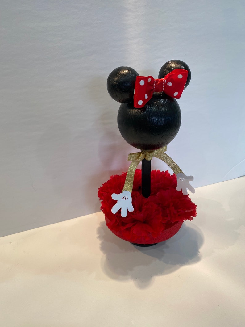 Pode incluir: Figura de Minnie Mouse preta e branca com um la&ccedil;o vermelho e uma saia de cravos vermelhos. A figura est&aacute; em p&eacute; sobre uma base preta.