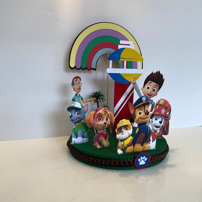 Puede incluir: Un adorno para pastel con tem&aacute;tica de Patrulla Canina con un arco&iacute;ris, un faro y personajes del programa. Los personajes incluyen a Chase, Skye, Marshall, Rocky y Zuma. El adorno es perfecto para una fiesta de cumplea&ntilde;os con tem&aacute;tica de Patrulla Canina.