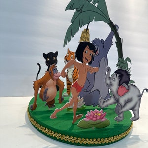 Peut inclure: Un topper de g&acirc;teau sur le th&egrave;me de la jungle vert et marron repr&eacute;sentant Mowgli du Livre de la Jungle de Disney. Le topper comprend Mowgli, Baloo l'ours, Shere Khan le tigre, Kaa le python, King Louie l'orang-outan et Bagheera la panth&egrave;re.