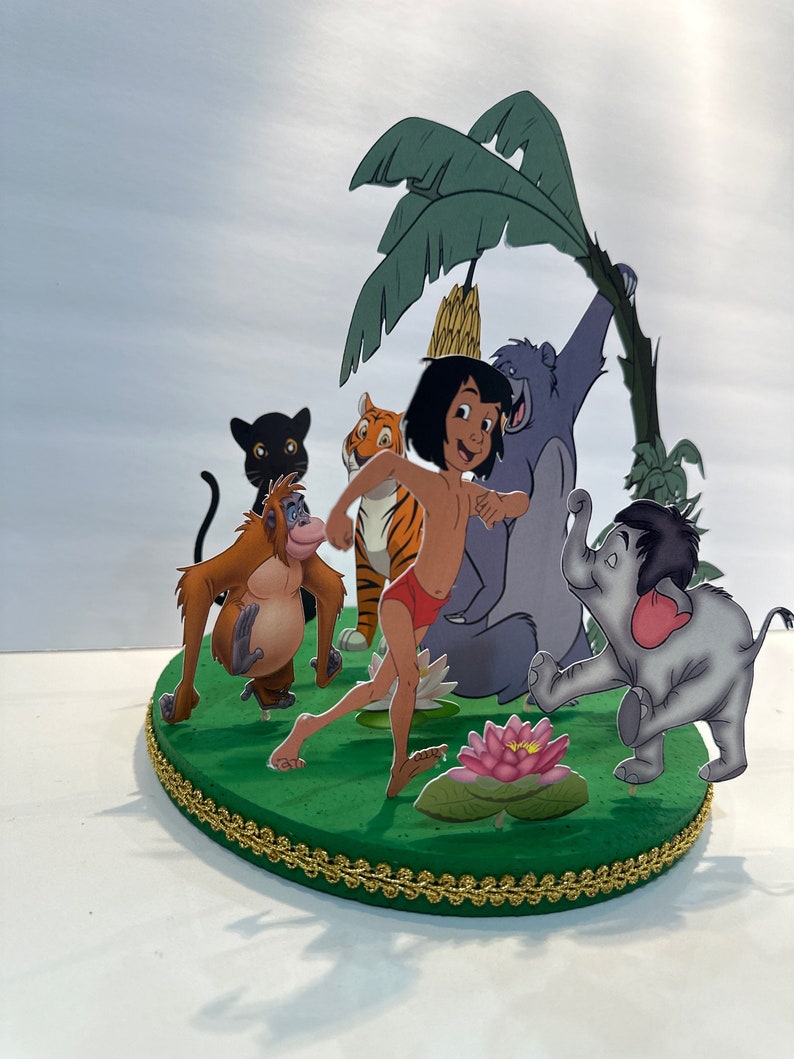 Peut inclure: Un topper de g&acirc;teau sur le th&egrave;me de la jungle vert et marron repr&eacute;sentant Mowgli du Livre de la Jungle de Disney. Le topper comprend Mowgli, Baloo l'ours, Shere Khan le tigre, Kaa le python, King Louie l'orang-outan et Bagheera la panth&egrave;re.