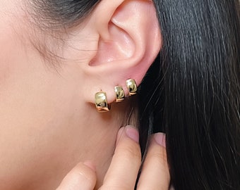May include: A close-up of a person's ear with four gold hoop earrings of varying sizes. The earrings are all smooth and have a shiny finish.