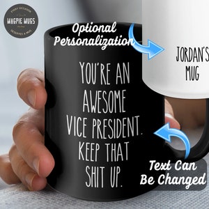 May include: Black coffee mug with white text that reads "You're an awesome Vice President. Keep that shit up." The mug has a black handle and is held by a hand. The text "Jordan's Mug" is visible on a white mug in the background.