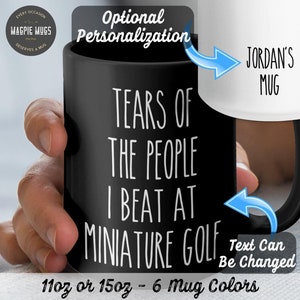 May include: Black ceramic mug with white text that reads "Tears of the people I beat at miniature golf". The text "Jordan's Mug" is visible on a white mug in the background. The mug is 11 oz or 15 oz and comes in 6 colors.