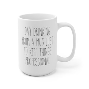 May include: White ceramic mug with a large handle. The mug features the text "DAY DRINKING FROM A MUG JUST TO KEEP THINGS PROFESSIONAL" in black, handwritten-style lettering. The mug is a standard size for coffee or tea.