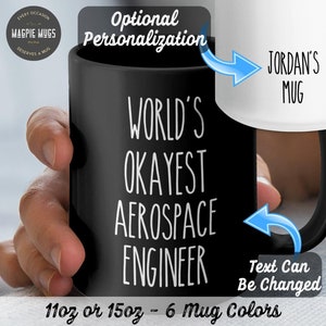 May include: Black ceramic mug with white text that reads "World's Okayest Aerospace Engineer". The text "Jordan's Mug" is visible on a white mug in the background. The mug is 11 oz or 15 oz and comes in 6 colors.