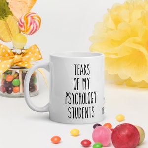 May include: White ceramic coffee mug with black text that reads "Tears of my Psychology Students".