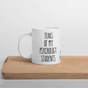 May include: White ceramic coffee mug with black text that reads "Tears of my Psychology Students".