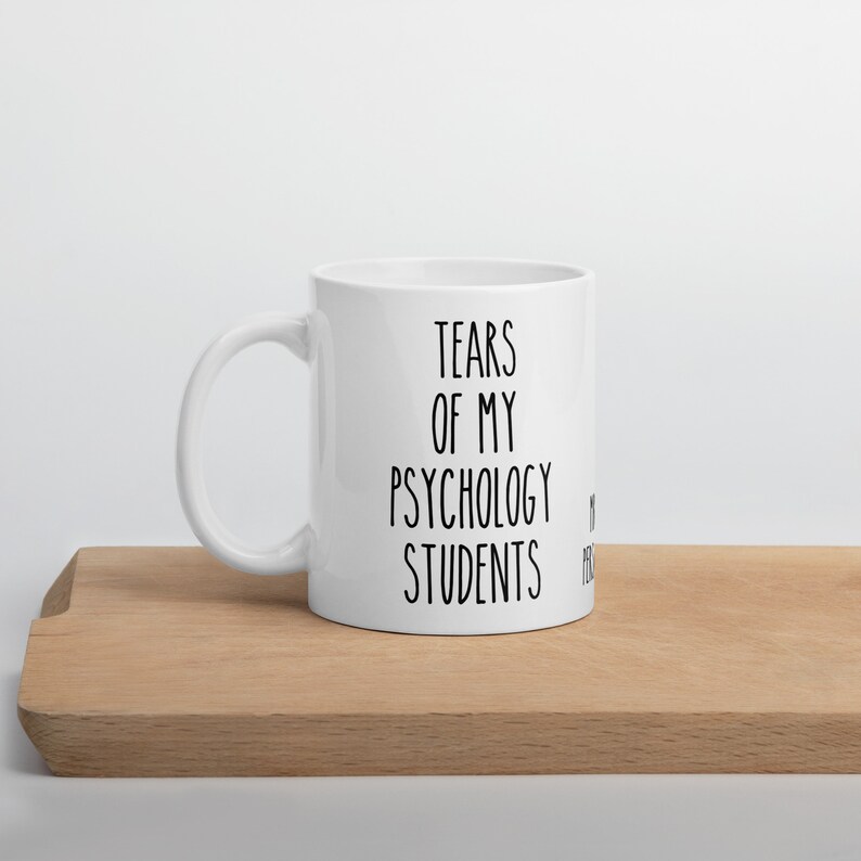 May include: White ceramic coffee mug with black text that reads "Tears of my Psychology Students".