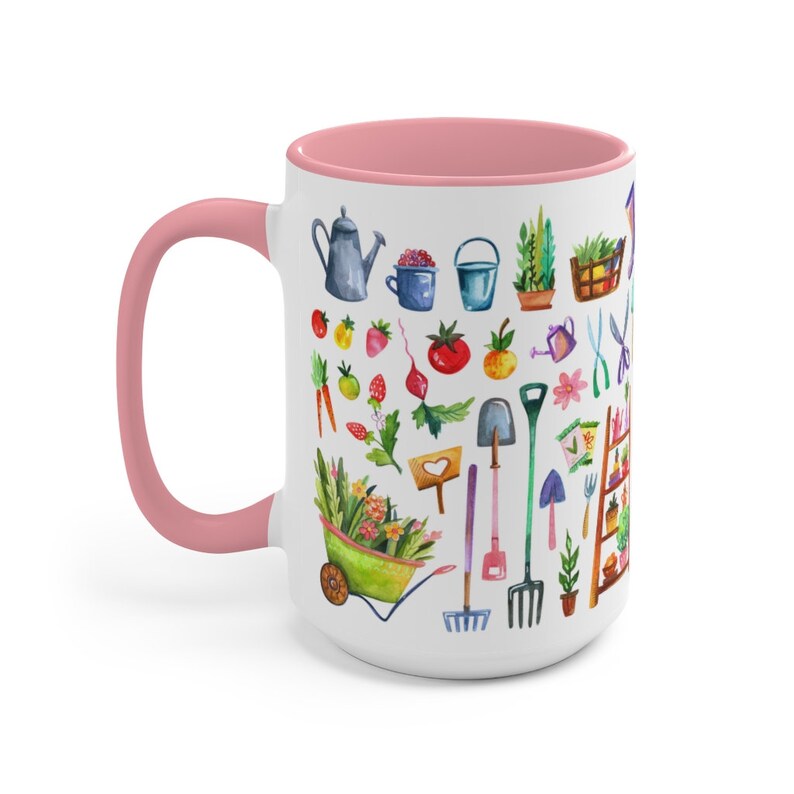 May include: White ceramic mug with a pink interior and handle. The mug is decorated with a watercolor illustration of gardening tools, vegetables, and plants. The design includes a wheelbarrow, watering can, and various gardening implements.