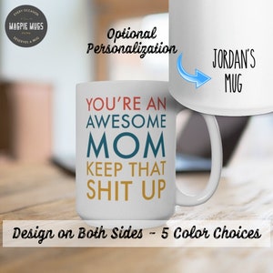 K&ouml;nnte beinhalten: Eine wei&szlig;e Keramik-Kaffeetasse mit dem Text "You're an Awesome Mom Keep That Shit Up" in bunten Buchstaben. Die Tasse hat einen Henkel und wird auf einer Holzoberfl&auml;che gezeigt. Der Text "Optionale Personalisierung" ist im Hintergrund sichtbar. Die Tasse ist in 5 Farben erh&auml;ltlich.
