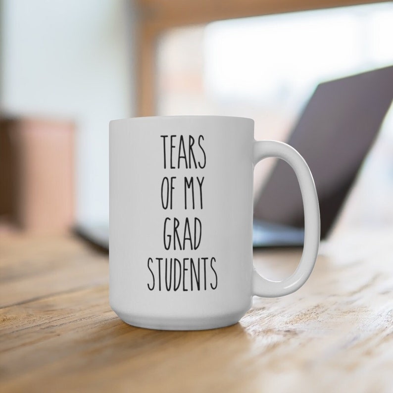 May include: White ceramic coffee mug with black text that reads "Tears of my grad students".