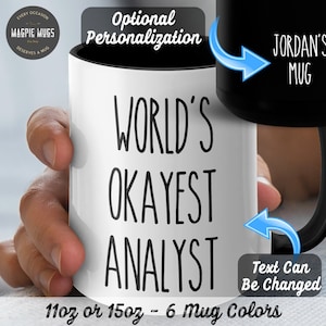 May include: White ceramic mug with black text that reads "World's Okayest Analyst". The mug is 11 oz or 15 oz and comes in 6 colours. The text can be personalised.