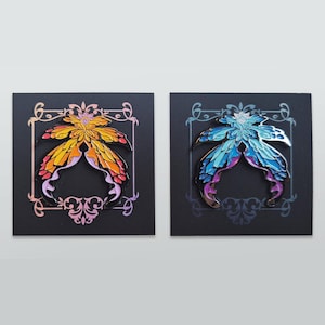 May include: Two butterfly-shaped enamel pins. One pin features a gradient of yellow, orange, and pink, while the other showcases blue, purple, and silver hues. Both are set against a black background with decorative borders.