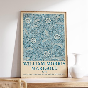 Op de afbeelding: Een ingelijste kunstdruk met een teal bloemenpatroon en witte accenten. De print bevat de tekst "WILLIAM MORRIS MARIGOLD 1875 ORIGINAL FROM THE SMITHSONIAN INSTITUTION" in een crème banner. Het kunstwerk staat op een houten plank.