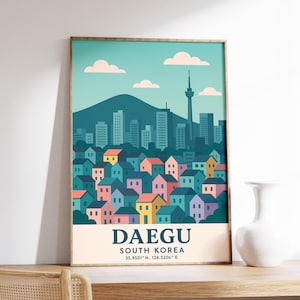 May include: A framed art print featuring a colorful illustration of Daegu, South Korea. The artwork depicts a cityscape with buildings, a mountain, and a tower under a blue sky with clouds. The city's name and coordinates are printed at the bottom.