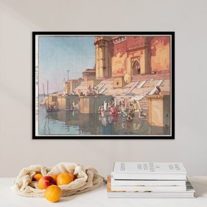 May include: A vintage woodblock print depicting a scene in India. The print shows a large building with steps leading down to a river. People are gathered on the steps and in the water, washing themselves. The print is framed in black.