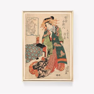 Könnte beinhalten: Ein Holzschnitt einer Frau in einem grün-roten Kimono, die einen Fächer hält. Die Frau steht vor einem Tisch mit einer Blumenvase. Der Druck ist in Gold gerahmt.