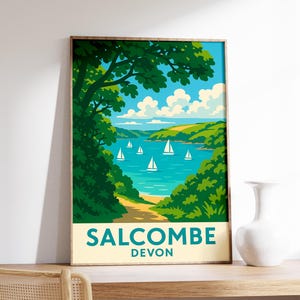 May include: A framed art print featuring a coastal scene with sailboats on the water. The artwork has a vintage travel poster style, with the text "SALCOMBE DEVON" at the bottom. The color palette includes blues, greens, and beige.