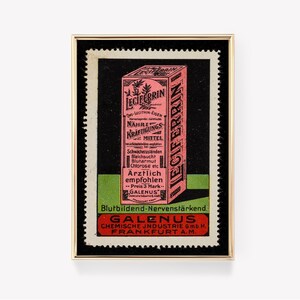 Könnte beinhalten: Eine Vintage-Werbung für Leciferrin, ein blutbildendes und nervenstärkendes Nahrungsergänzungsmittel. Die Anzeige zeigt eine rosa und weiße Schachtel mit dem Produktnamen und einer Beschreibung der Vorteile. Die Anzeige ist in Gold gerahmt und hat einen schwarzen Hintergrund.