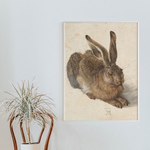 May include: A detailed drawing of a brown hare, lying down with its head turned to the side. The hare has long ears and a white patch on its chest. The drawing is on a light brown paper with the date "1502" and the artist's initials "A.D." in the bottom right corner.