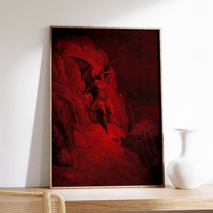 May include: A red and black framed print of a winged figure with a red background. The figure is standing on a rocky cliff and appears to be looking up.