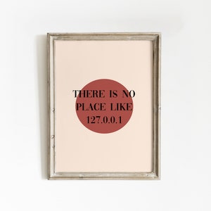 May include: A framed print with a red circle and the text "THERE IS NO PLACE LIKE 127.0.0.1" on a light pink background.