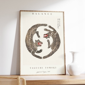 May include: A black and white poster with the word "BALANCE" in brown text at the top. The poster features a circular design of two black and white tigers facing each other with their mouths open. The poster is framed in a light brown wood frame. The text "TAGUCHI TOMOKI" is in brown text at the bottom of the poster, with the words "japanese tigers 1960" in smaller brown text below.