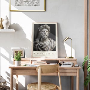 May include: A framed poster of a bust of Marcus Aurelius, a Roman emperor and philosopher, with the text "Marcus Aurelius" below the image. The poster is hanging on a white wall above a wooden desk with a lamp, books, and a potted plant.