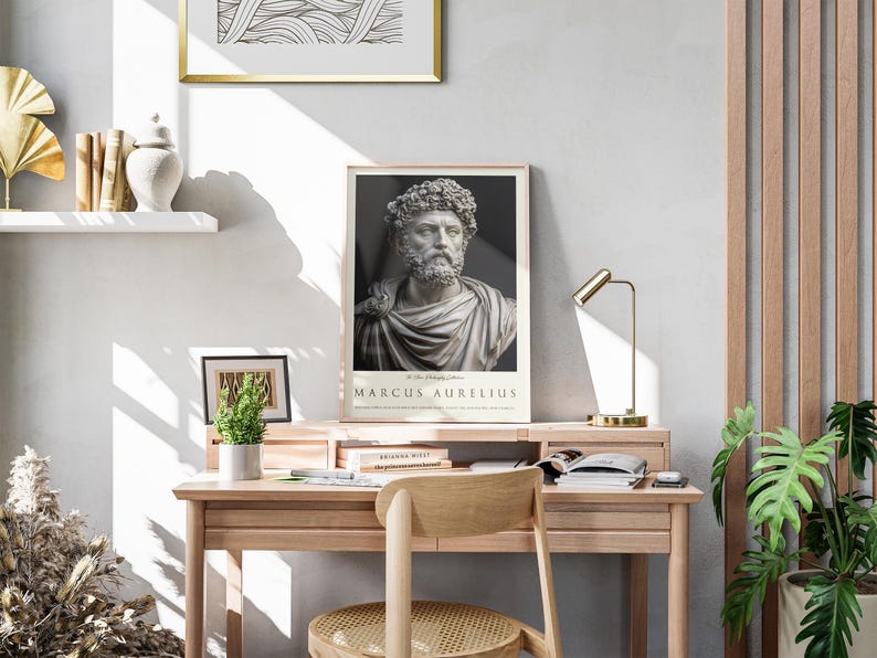 May include: A framed poster of a bust of Marcus Aurelius, a Roman emperor and philosopher, with the text "Marcus Aurelius" below the image. The poster is hanging on a white wall above a wooden desk with a lamp, books, and a potted plant.