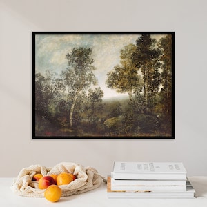 May include: A framed landscape painting depicting a forest scene with tall trees and a cloudy sky. The artwork is in a black frame and is displayed on a white surface. A mesh bag of oranges and peaches sits in front of the painting.