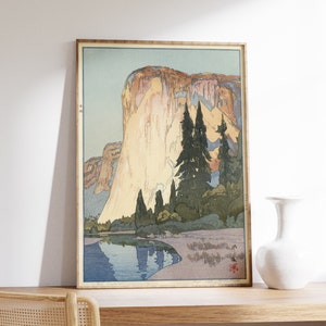 May include: A vintage woodblock print of a mountain landscape with a river in the foreground. The mountain is a light brown color with a blue sky behind it. The river is a light blue color and reflects the mountain. There are trees on the banks of the river.