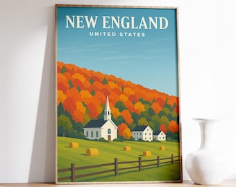 May include: A framed art print featuring a New England landscape. The artwork depicts a white church and houses set against a backdrop of fall foliage. The text "NEW ENGLAND UNITED STATES" is at the top. The print is displayed on a wooden surface.